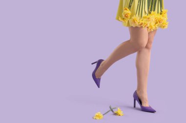 Yüksek topuklu kadın bacakları ve leylak arka planda nergis çiçekleri.