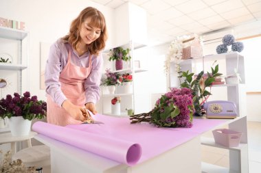 Çiçekçi kadın dükkanda leylak buketi için ambalaj kağıdı kesiyor.
