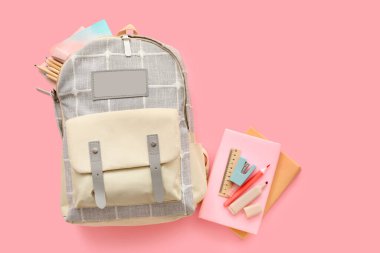 Kırtasiyeli gri okul çantası ve pembe arka plan kitapları.