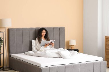 Genç Afro-Amerikalı kadın evdeki yumuşak yatakta dergi okuyor.