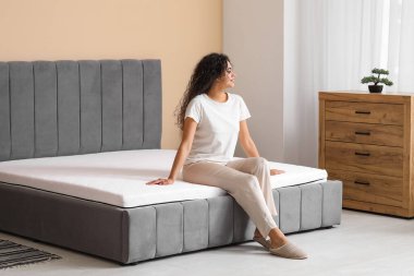 Genç Afro-Amerikalı kadın yatak odasında yumuşak bir yatakta oturuyor.