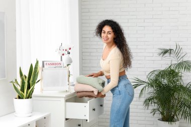 Güzel, genç, mutlu, Afro-Amerikan bir kadın evde temiz giysiler giyiyor.