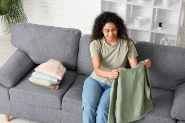 Güzel, genç, mutlu, Afro-Amerikan kadın. Temiz giysileri evde katlıyor.