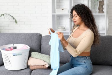 Çamaşır sepetiyle evde temiz giysileri katlayan güzel, mutlu, Afro-Amerikalı bir kadın.