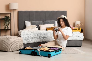 Kameralı güzel, genç ve mutlu bir kadın. Evdeki bavullardan yaz kıyafetlerini çıkarıyor.