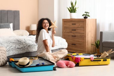 Evdeki bavullardan deniz yıldızlı güzel, genç ve mutlu bir kadın.