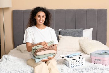 Güzel, genç, mutlu, Afro-Amerikan bir kadın yatak odasında temiz giysiler katlıyor.