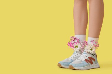 Sarı arka planda farklı çiçekler olan spor ayakkabılı kadın bacakları.