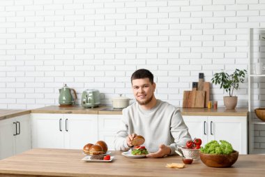 Genç adam mutfakta lezzetli hamburgerler yapıyor.