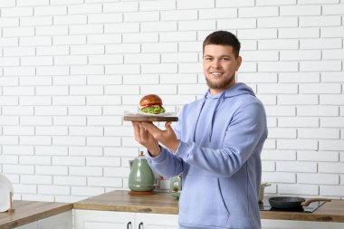 Genç adam mutfakta lezzetli bir burgerle tahta tutuyor.