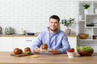 Mutfakta lezzetli hamburgerle tabağı tutan genç adam.