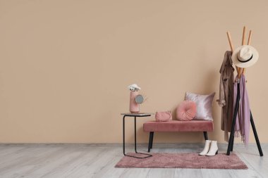 Samimi bir bank, elbise ve halı ile bej duvarın yanında.