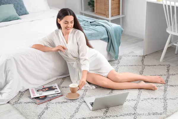Evinde bir fincan sıcak kahve ve dizüstü bilgisayarı olan güzel bir kadın.