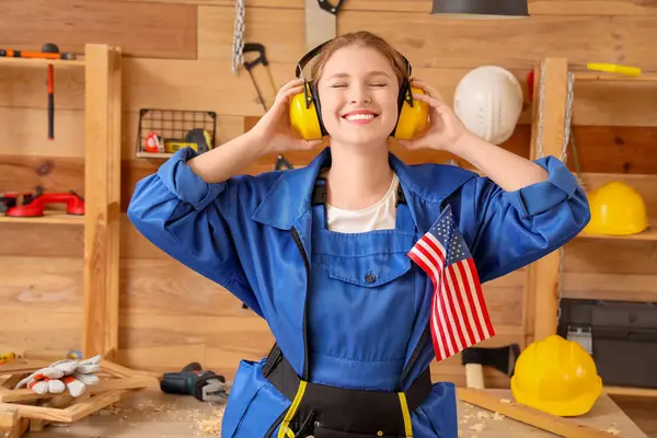 Atölyede kulaklıkları ve ABD bayrağı olan genç bir kadın marangoz. İşçi Bayramı kutlamaları
