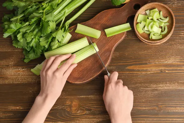 Ahşap arka planda taze yeşil kereviz kesen kadın.