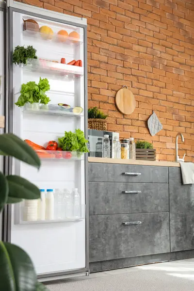 Mutfaktaki tuğla duvarın yanında taze yiyeceklerle dolu bir buzdolabı.