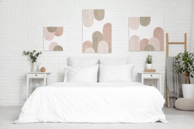 Güzel bir yatak odası, rahat bir yatak odası, komodinleri ve beyaz tuğlalı duvarda resimleri var.