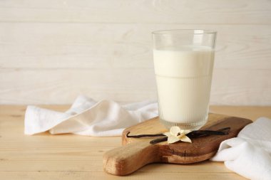 Bir bardak taze vanilya sütü, sopalı ve çiçekli ahşap masa