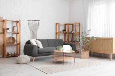 Oturma odasının içinde siyah kanepe, çekmeceler, sehpa ve zeytin ağacı var.