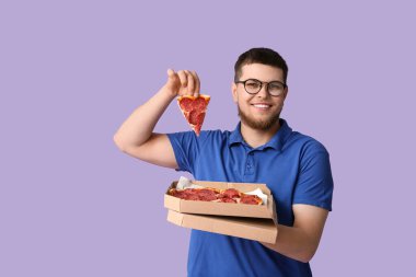Elinde leylak arkaplanda lezzetli pepperonili pizza olan karton kutu tutan genç adam.