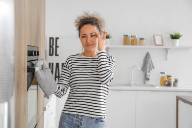 Mutfakta yemek pişirirken parmağında kırmızı ip olan düşünceli orta yaşlı bir kadın. Hatırlatma konsepti