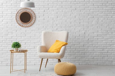 Sarı yastıklı koltuk, puf ve beyaz tuğla duvarın yanındaki sehpa.