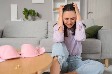 Crying young woman after finding mistress's bra at home. Cheating concept