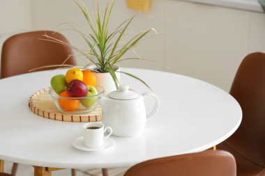 Mutfaktaki yemek masasında bir fincan kahve ve meyveli çaydanlık.