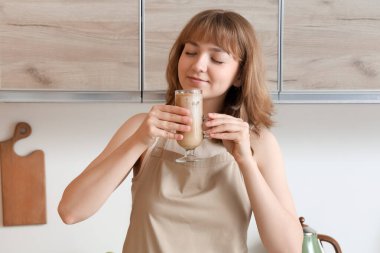 Mutfakta bir bardak lezzetli buzlu latte ile genç bir kadın.