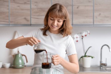 Genç bir kadın mutfaktaki buzla bardağa kahve dolduruyor.