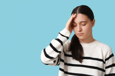 Güzel genç bayan mavi arka planda baş ağrısı çekiyor.