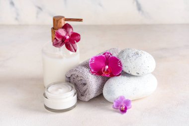 Spa taşları, krem, losyon, havlu ve orkide çiçekleri açık arkaplanda