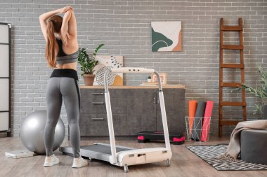 Koşu bandının yanında antrenman yapan sportif bir kadın.