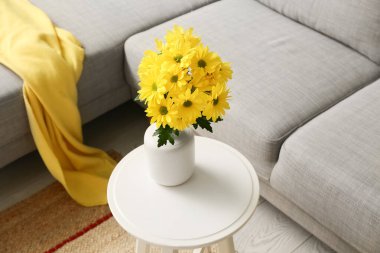 Şık oturma odasının içinde rahat bir kanepe, kahve masasında çiçekler ve ekoseli vazo, yakın çekim.