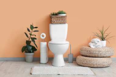 Tuvaletin içinde bej duvarın yanında klozet, puf ve bitkiler var.