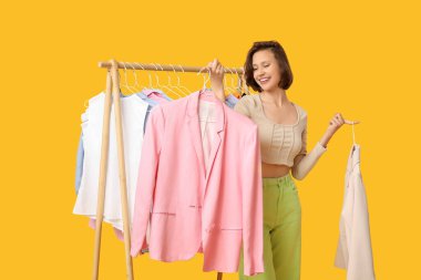 Güzel bir genç kadın sarı arka planda elbise seçiyor.