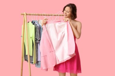 Farklı giysileri olan güzel bir kadın pembe arka planda ceket seçiyor.