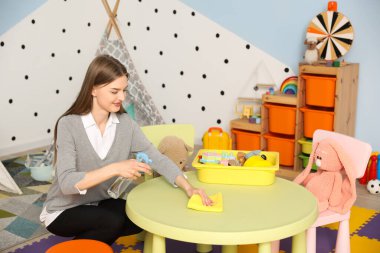 Anaokulundaki kadın kreş öğretmeni masasını temizliyor.