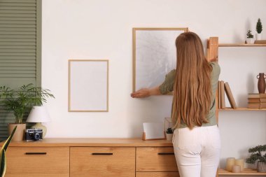 Modern oturma odasındaki beyaz duvara boş çerçeveler asan genç bir kadın.