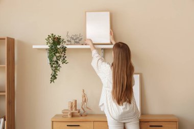 Modern oturma odasındaki bej duvara boş çerçeveler asan genç bir kadın.