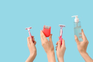 Mavi arka planda modern epilatör, ustura ve bir şişe kozmetik ürünü olan kadın elleri.