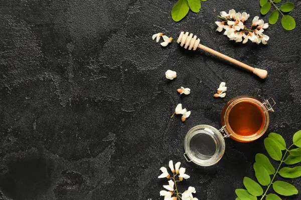 Akasya çiçekli tatlı bal kavanozu ve siyah arkaplanlı dipper.