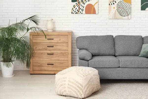 İçinde rahat bir kanepe, puf, çekmeceler ve resimler olan güzel bir oturma odası.