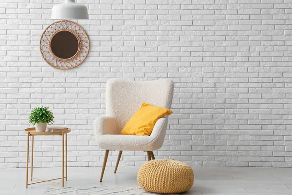 Sarı yastıklı koltuk, puf ve beyaz tuğla duvarın yanındaki sehpa.