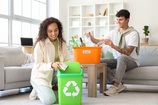 Молодая пара с мусорными контейнерами разбирает мусор дома. Концепция переработки отходов