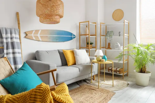 Rahat kanepesi, sehpası, raf ünitesi ve sörf tahtasıyla oturma odasının içi aydınlık.