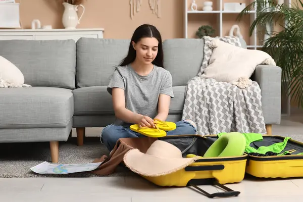 Evde yerde parmak arası terlikleri bavulda toplayan genç bir kadın. Yaz yolculuğu konsepti