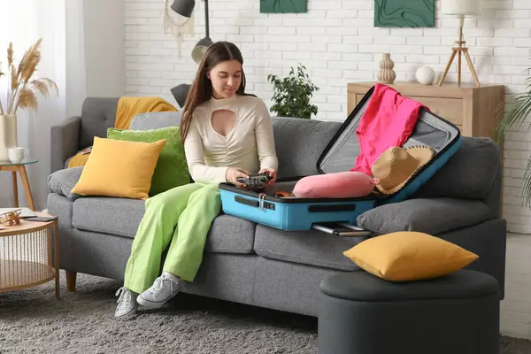 Evdeki kanepede fotoğraf makinesini valize koyan genç bir kadın. Yaz yolculuğu konsepti