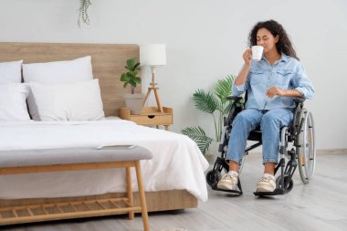 Tekerlekli sandalyedeki genç Afro-Amerikalı kadın evinde bir fincan kahveyle