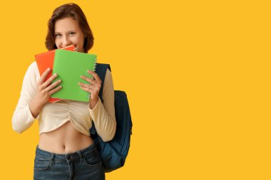 Sarı arka planda not defterleri ve sırt çantasıyla güzel bir kız öğrenci.